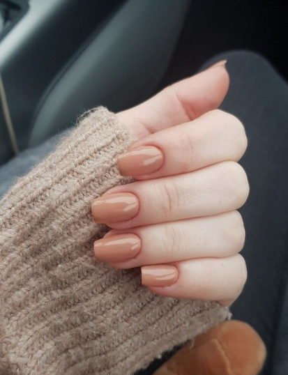 25 Nail Colors That Make Hands Look Younger A close-up of a hand wearing a warm beige sweater showcasing glossy nude-brown square nails, demonstrating nail colors that make hands look younger.