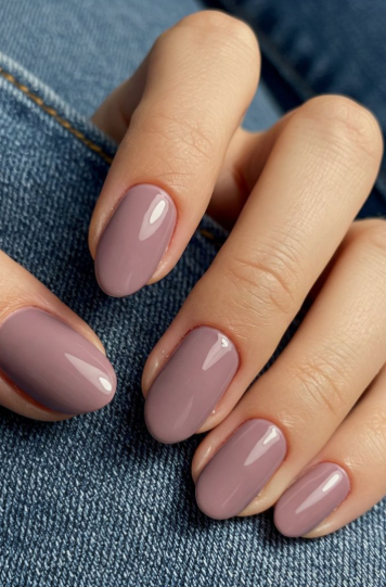 25 Nail Colors That Make Hands Look Younger A close-up of a hand resting on blue denim, featuring elegant oval-shaped mauve polish as one of the best nail colors that make hands look younger.