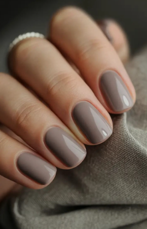 25 Nail Colors That Make Hands Look Younger A close-up of a hand with glossy taupe-brown square nails touching textured fabric, showcasing nail colors that make hands look younger.