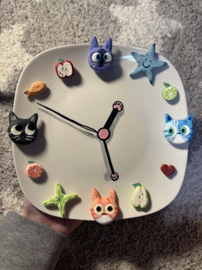 A square handmade wall clock featuring colorful air dry clay ideas, decorated with sculpted cat faces, fruits, and stars marking the hours.