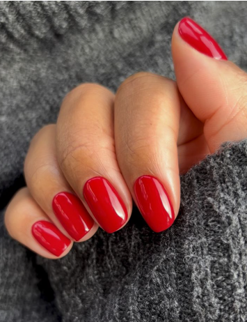 25 Nail Colors That Make Hands Look Younger A hand wearing a textured gray sweater showcasing classic glossy red square nails, illustrating timeless nail colors that make hands look younger.