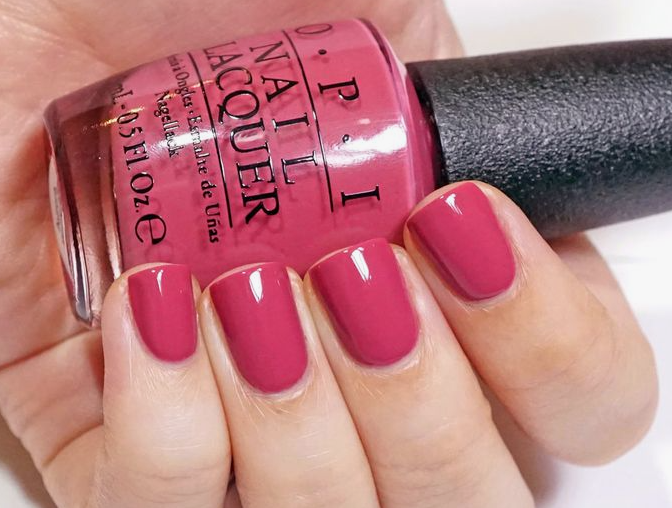25 Nail Colors That Make Hands Look Younger A close-up of a hand holding an OPI nail lacquer bottle, showcasing vibrant berry-pink polish as one of the best nail colors that make hands look younger.