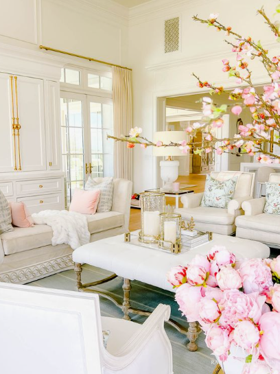 spring living room decor featuring an elegant white upholstered coffee table styled with glass candle holders and a vibrant arrangement of pink peonies