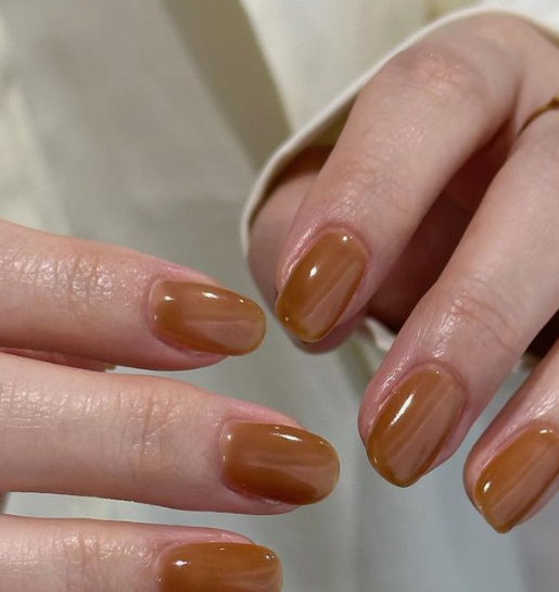 25 Nail Colors That Make Hands Look Younger A close-up of hands featuring glossy caramel-brown short nails, showcasing trendy nail colors that make hands look younger.