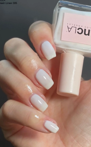 25 Nail Colors That Make Hands Look Younger A close-up of a hand holding anncLA Fresh Linen nail polish bottle, featuring milky white square nails as clean and fresh nail colors that make hands look younger.