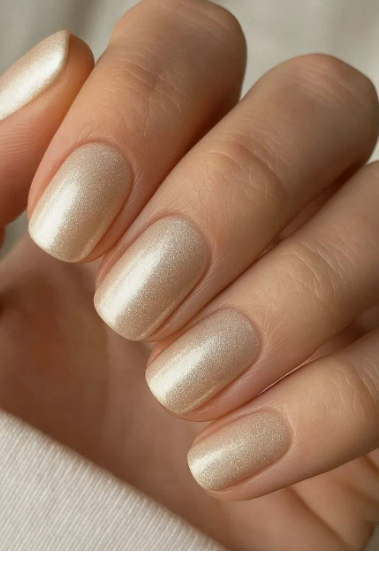 25 Nail Colors That Make Hands Look Younger A close-up of short, squared shimmering pearl-champagne nails that capture the light, representing luminous nail colors that make hands look younger.