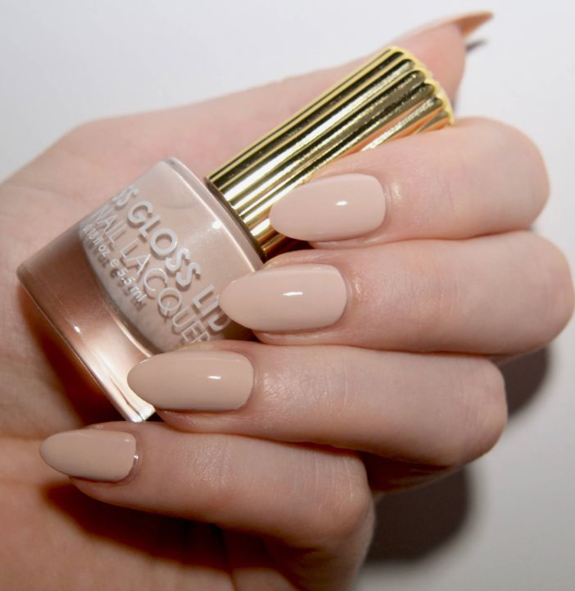 25 Nail Colors That Make Hands Look Younger A close-up of a hand holding a gloss-up nail lacquer bottle, showcasing creamy nude oval nails as sophisticated nail colors that make hands look younger.