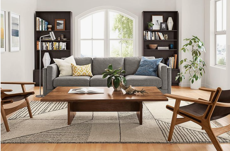 A well-organized living room featuring a grey sofa, matching dark wood bookshelves framing an arched window, a wooden coffee table, and mid-century modern accent chairs, presenting inspiring small apartment decor ideas.