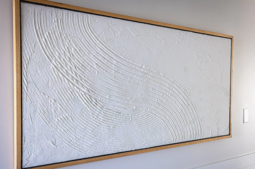 A large, modern abstract textured white canvas painting framed in light wood, featuring sweeping combed plaster patterns that exemplify elegant DIY crafts that look expensive.