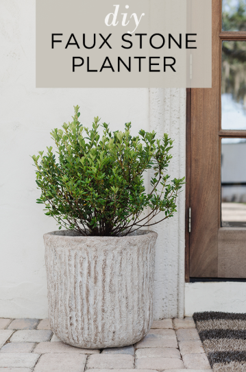 A textured, weathered faux stone planter holding a lush green shrub by a wooden front door, highlighting gorgeous DIY crafts that look expensive for outdoor entryways.