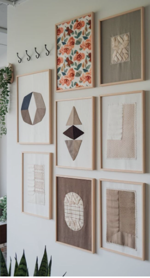 A gallery wall featuring framed textile art pieces with neutral fabrics, geometric stitching, and a floral pattern, showcasing incredible DIY crafts that look expensive for modern home decor.