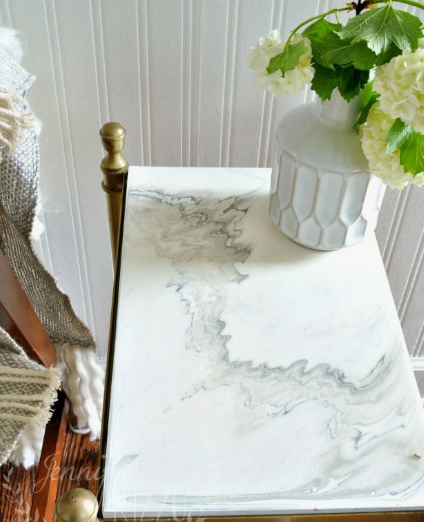 A small side table featuring a smooth faux marble top with grey and white veining, styled with a white textured vase and green flowers, demonstrating luxurious DIY crafts that look expensive for home interiors.