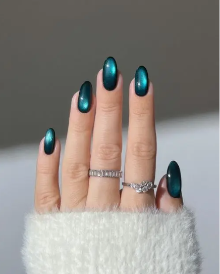 2026 Beauty Trends That Are Actually Worth Trying A close-up of oval-shaped nails finished with a mesmerizing dark green magnetic cat-eye polish and styled with sparkling rings, showcasing trending 2026 beauty trends for statement manicures.