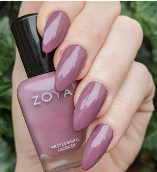 30 Classy Nail Colors for Mature Hands A hand holding a Zoya professional lacquer bottle, showcasing classy nail colors for mature hands with glossy almond-shaped mauve-purple nails.