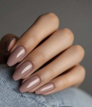 30 Classy Nail Colors for Mature Hands A close-up of a hand showcasing classy nail colors for mature hands, featuring glossy taupe-beige coffin nails resting against denim fabric.