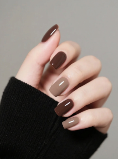 30 Classy Nail Colors for Mature Hands Hands showcasing classy nail colors for mature hands, featuring a glossy gradient manicure in shades of brown and taupe on short square nails against a black sweater sleeve.