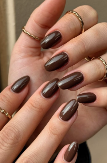 30 Classy Nail Colors for Mature Hands Hands showcasing classy nail colors for mature hands, featuring glossy espresso-brown oval nails styled with minimalist twisted gold rings.