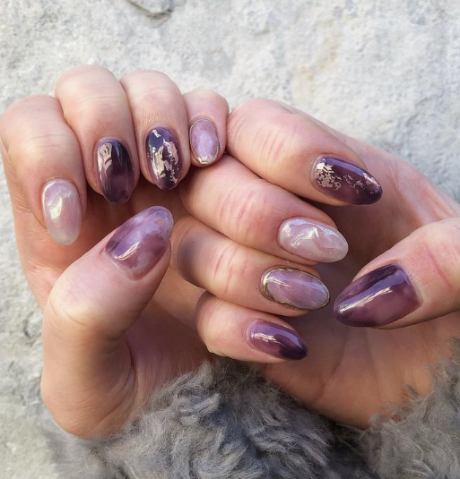 30 Classy Nail Colors for Mature Hands Hands showcasing classy nail colors for mature hands, featuring glossy purple and pearl watercolor marble nails accented with delicate gold foil flakes.