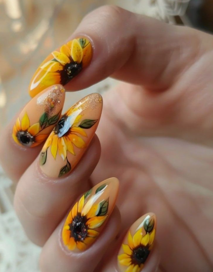 24 Sunflower Nail Ideas for a Bright, Cheerful Manicure sunflower nail ideas featuring almond-shaped nails painted with detailed yellow and brown sunflowers, green leaves, and subtle glitter accents on a nude base.
