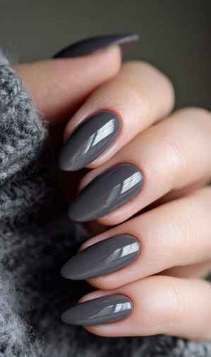 30 Classy Nail Colors for Mature Hands Hands showcasing classy nail colors for mature hands, featuring glossy charcoal gray oval nails paired with a cozy gray knit sweater.