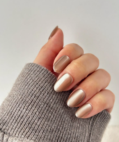 30 Classy Nail Colors for Mature Hands Hands showcasing classy nail colors for mature hands, featuring glossy metallic champagne and taupe cat-eye oval nails paired with a gray ribbed sweater.