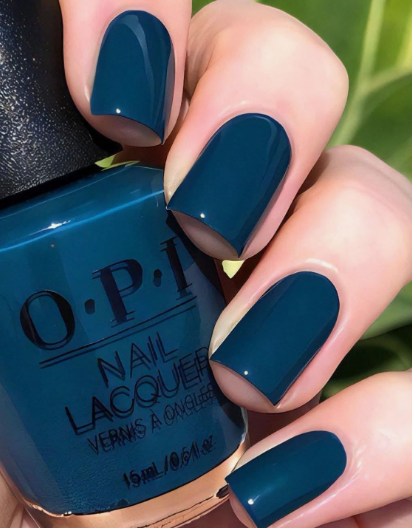 30 Classy Nail Colors for Mature Hands A hand holding an OPI nail polish bottle, showcasing classy nail colors for mature hands featuring a glossy deep teal-blue manicure on short square nails.