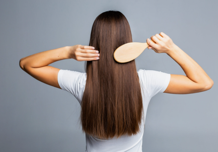 "A woman brushing her long brown hair with a wooden brush as part of her Sunday beauty reset routine."