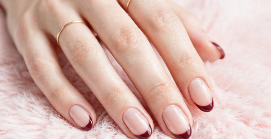 Glossy wine red french nails ideas featuring neatly manicured oval nude nails with deep burgundy tips resting on soft pink faux fur.
