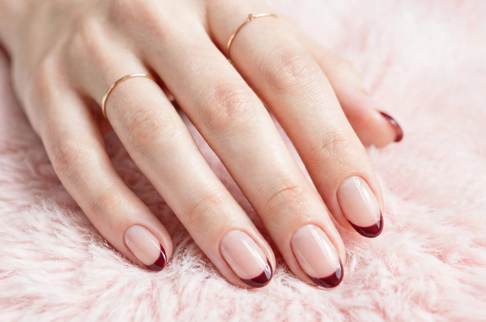 Glossy wine red french nails ideas featuring neatly manicured oval nude nails with deep burgundy tips resting on soft pink faux fur.