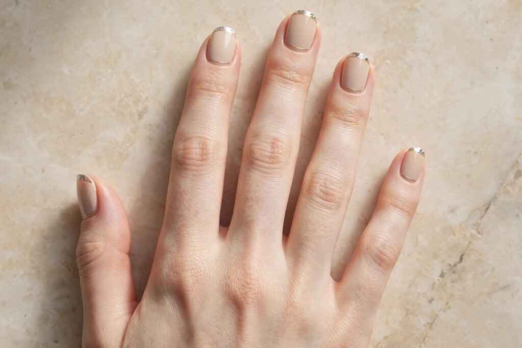 Short nail inspo 2026 showing neutral beige nude squoval nails with metallic silver chrome French tips and gold line borders.   
