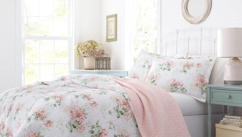 Floral pink and white quilted coverlet with matching pillow shams highlighting cottage bedding set ideas 2026 on a white wrought iron bed.