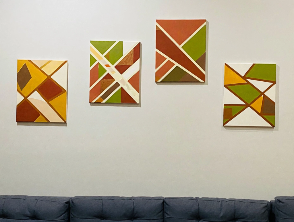 20 Retro Crafts to Try for a Creative Weekend Gallery wall set of four abstract geometric canvas paintings in mid-century earth tones of mustard yellow, olive green, rust, and cream, displayed above a sofa as inspiring retro crafts home wall decor.