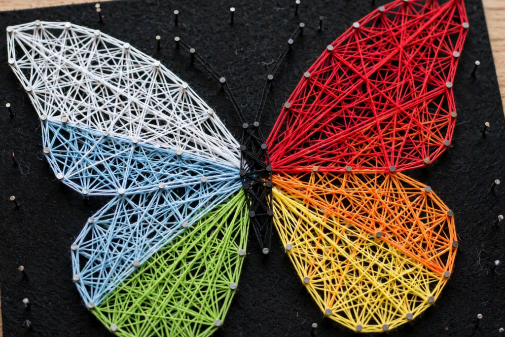 20 Retro Crafts to Try for a Creative Weekend DIY colorful butterfly string art crafted with nails and vibrant threads in rainbow shades of white, blue, green, yellow, and red on a black board, featuring creative retro crafts wall art.