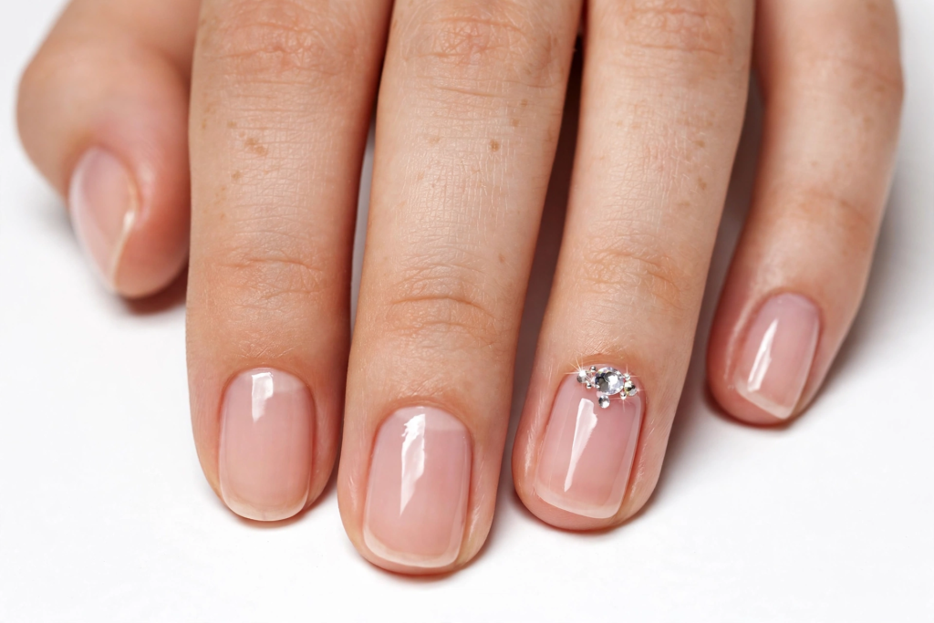 Minimalist sheer nude manicure showing easy 3D nail art designs with a single sparkling crystal rhinestone cluster at the cuticle of the accent nail.   