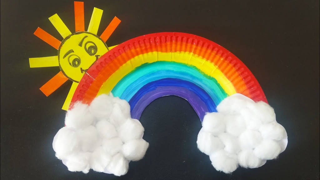 24 Preschool Seasonal Crafts for Spring, Summer, Fall & Winter A paper plate rainbow and sun craft with cotton ball clouds on a black background, representing preschool seasonal crafts.