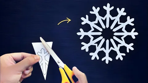 24 Preschool Seasonal Crafts for Spring, Summer, Fall & Winter Hands cutting folded paper with scissors to reveal an intricate paper snowflake, a winter activity for preschool seasonal crafts.