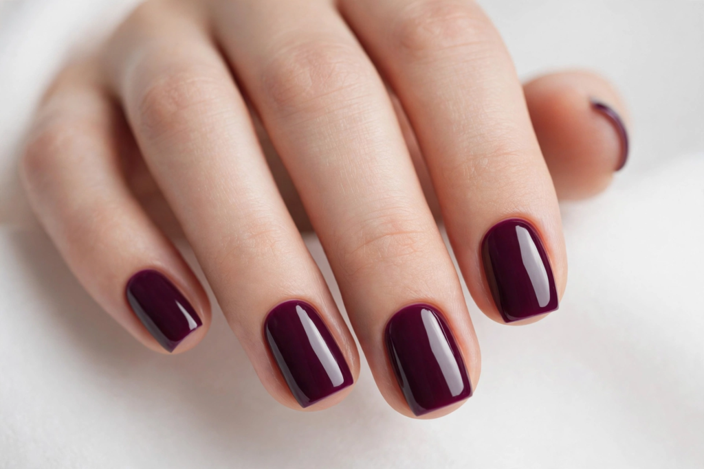 Glossy squoval dark plum manicure displayed against a white background, highlighting trendy fall plum nails 2026.   