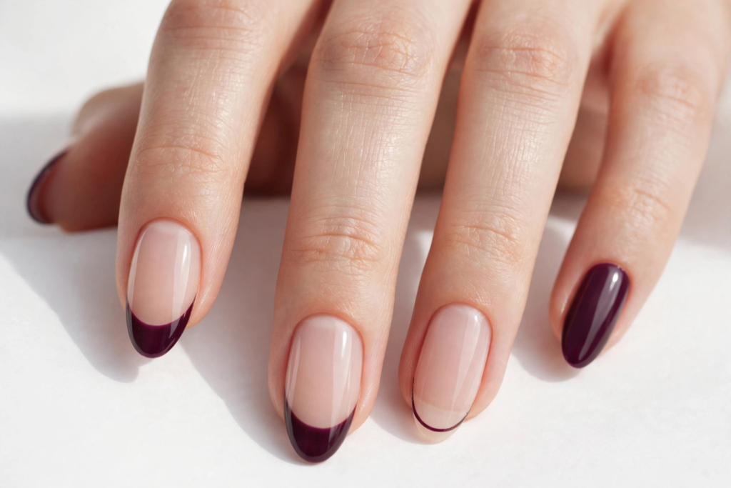 Elegant nude oval nails featuring deep purple French tips, a delicate outline accent, and a solid plum pinky nail for fall plum nails 2026.   