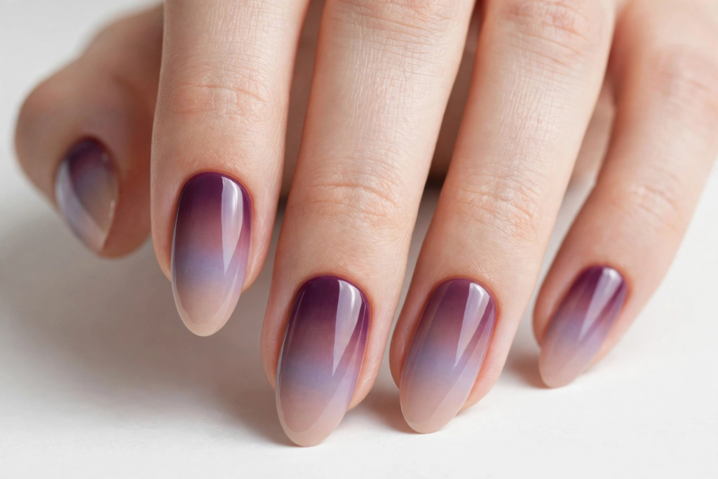 Glossy oval-shaped nails showcasing a reverse ombre gradient blending from deep plum at the cuticles to soft nude tips for fall plum nails 2026.