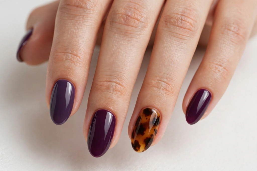 Glossy oval-shaped dark plum manicure featuring a trendy tortoiseshell accent nail on the ring finger for fall plum nails 2026.   