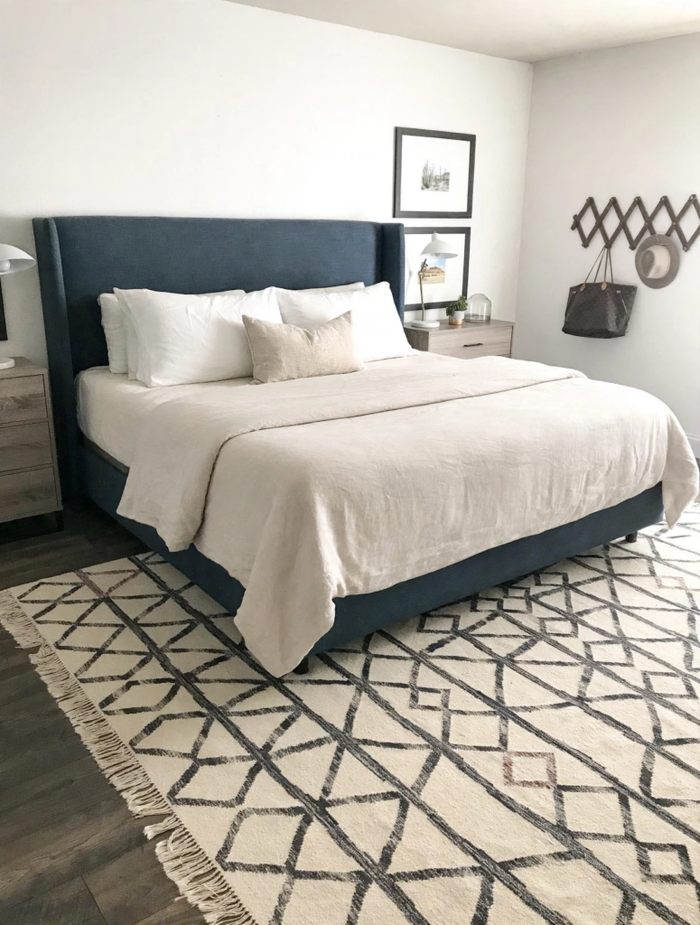 Modern bedroom design ideas showcasing a navy blue upholstered wingback bed with neutral linen bedding, wooden nightstands, and a cream geometric patterned area rug.