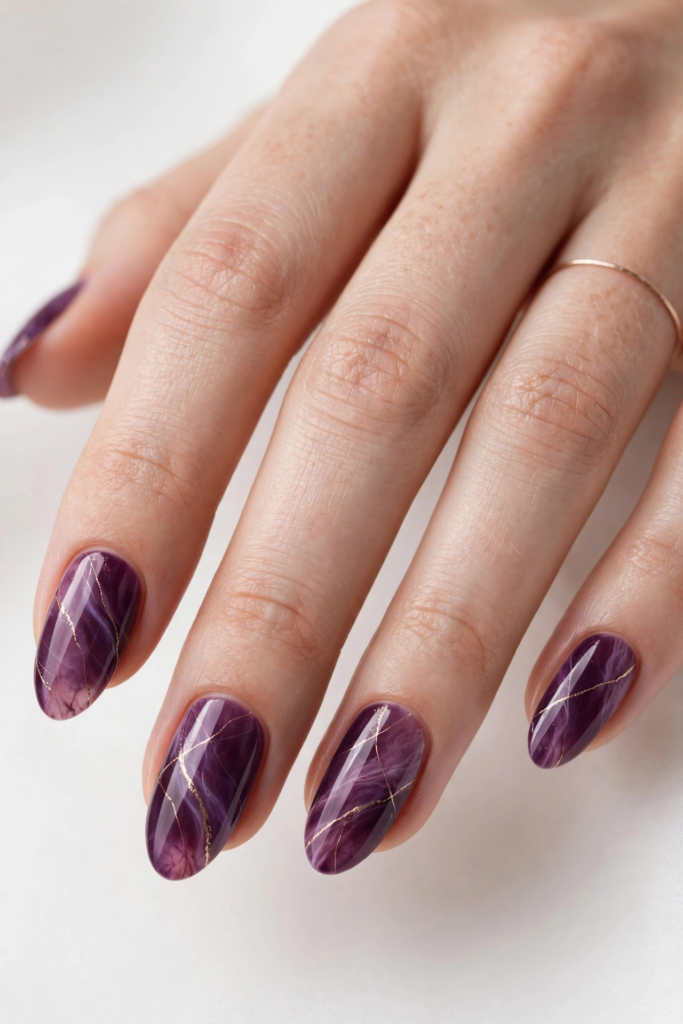 Glossy oval nails featuring a deep purple plum quartz marble effect with delicate metallic gold veining for fall plum nails 2026.   