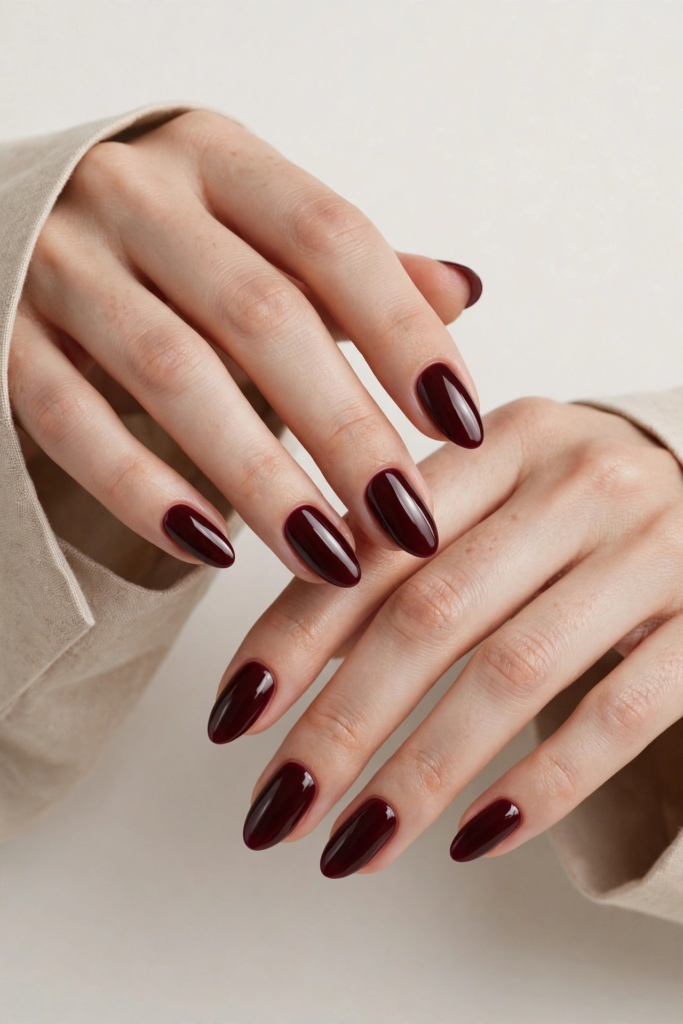 Elegant almond-shaped fall inspiration nails painted in a glossy, deep dark burgundy red polish.
