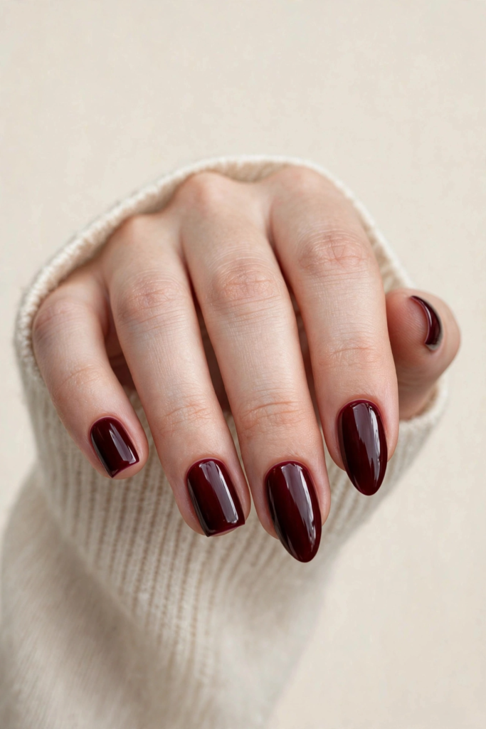 Fall nail inspo 2026 featuring high-gloss oxblood deep burgundy nails shown in both square and almond shapes with a cozy cream sweater.   