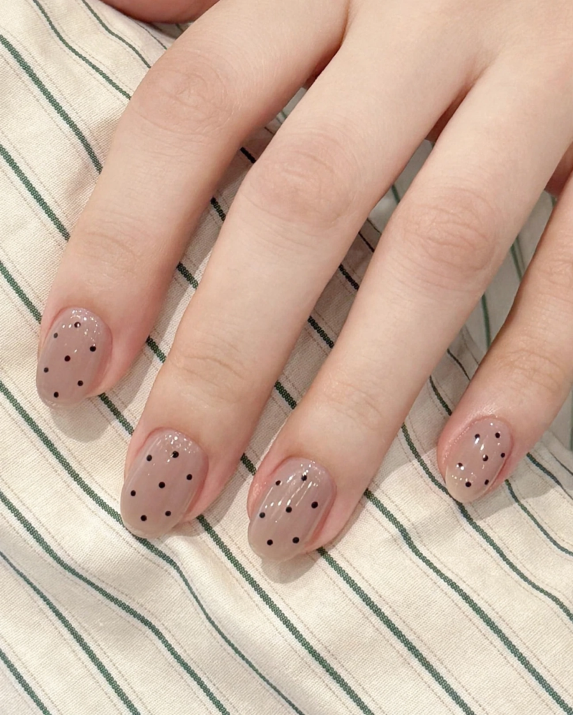 Short nail inspo 2026 showing minimalist black polka dots on sheer nude-beige glossy oval nails.   