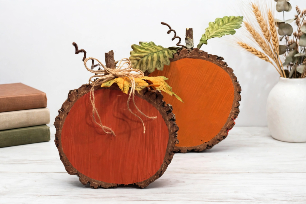 Pair of painted orange wood slice pumpkins with twig stems and twine bows as rustic fall crafts for adults.