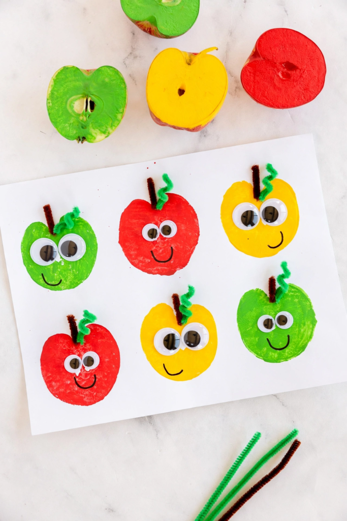 Colorful apple stamp art with googly eyes and pipe cleaner stems, a fun idea for fall crafts for kids.