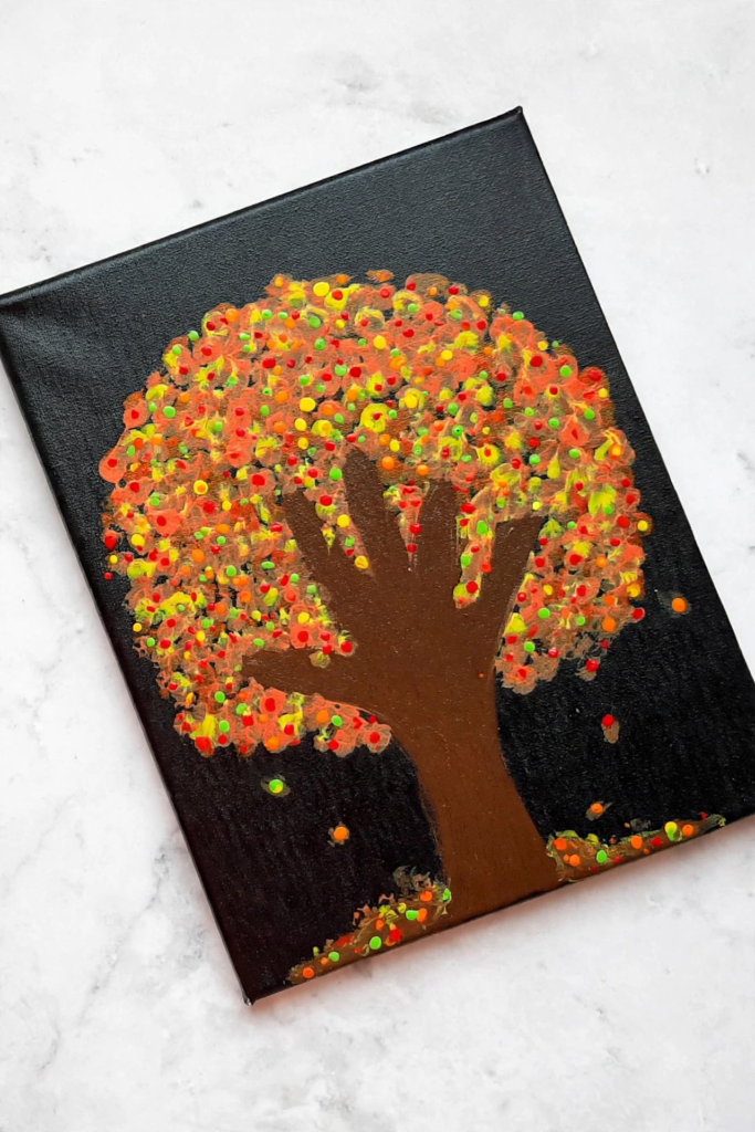 Handprint fall tree painting with colorful Q-tip painted leaves on a black canvas, a simple idea for fall crafts for kids.