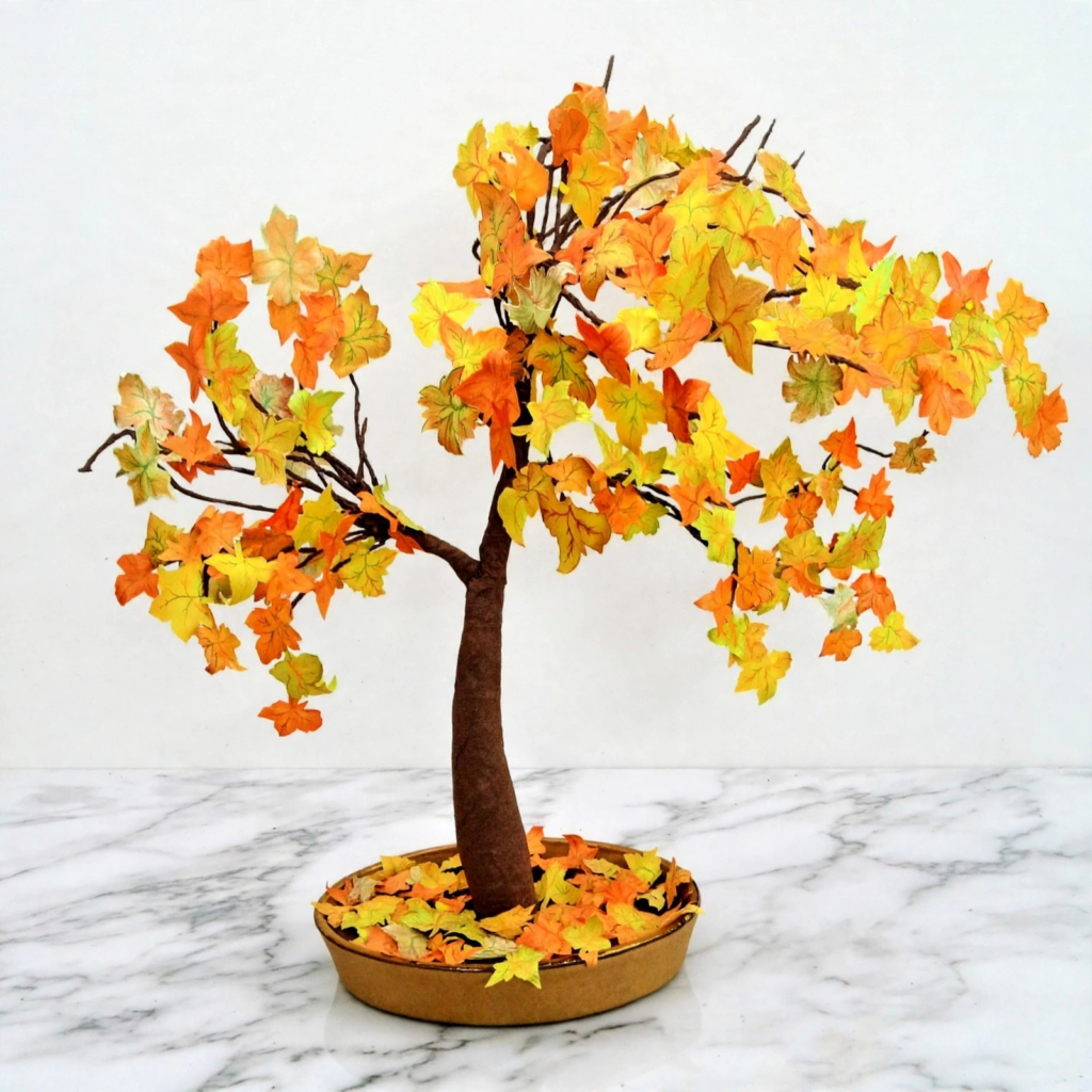 Miniature autumn bonsai tree craft with yellow and orange paper leaves in a ceramic dish, a creative idea for fall crafts for kids.   