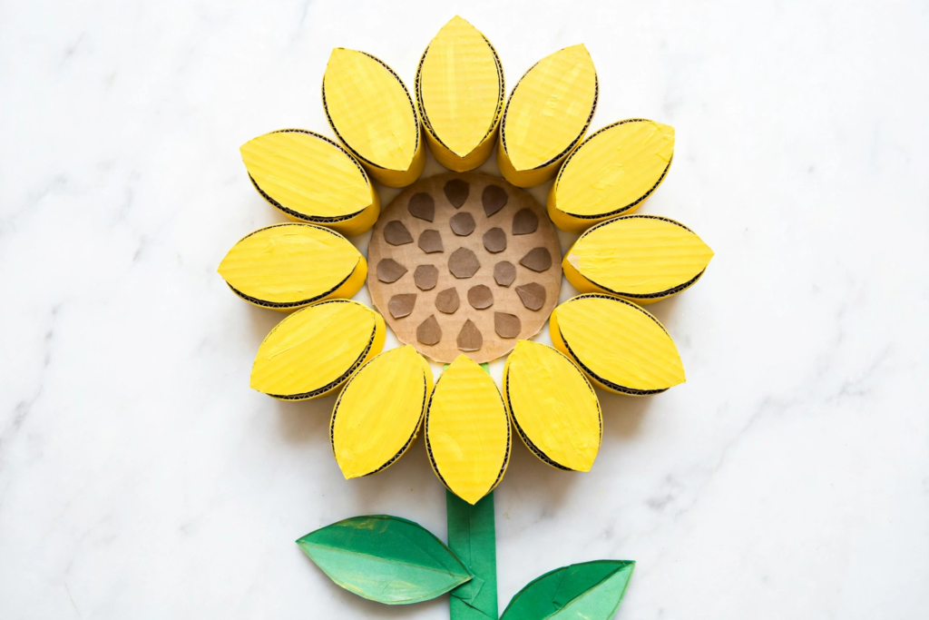 Cardboard roll sunflower craft painted yellow with a paper seed center and green stem, a creative idea for fall crafts for kids.   